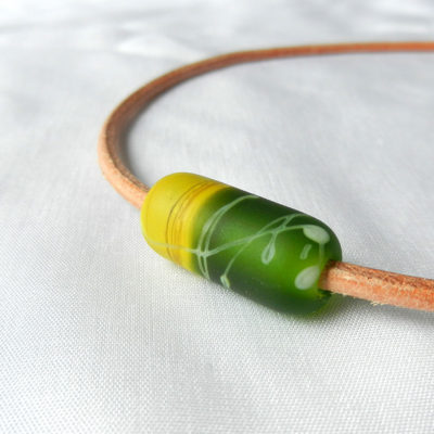 Einzelne Glasperle in Walzenform, handgefertigtes Unikat von schmuckes Glas. Glasperle in zwei Grün-tönen. Hellbraunes Lederband.